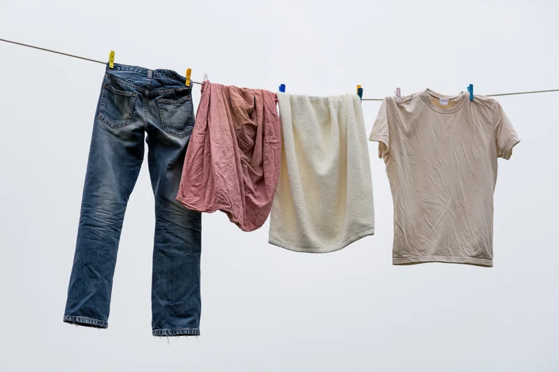 Blue jeans, pink cloth, cream towel and beige tshirt hanging on a clothesline against a plain sky