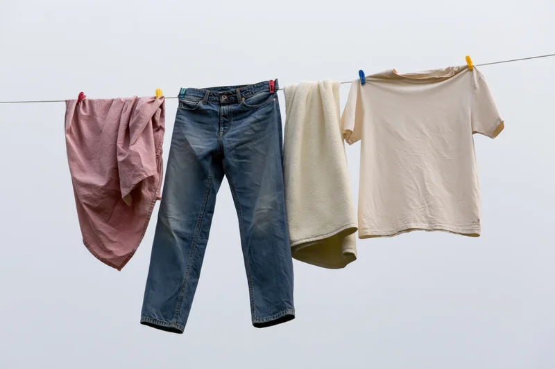 Blue jeans, pink cloth, cream towel and beige tshirt hanging on a clothesline against a pale sky
