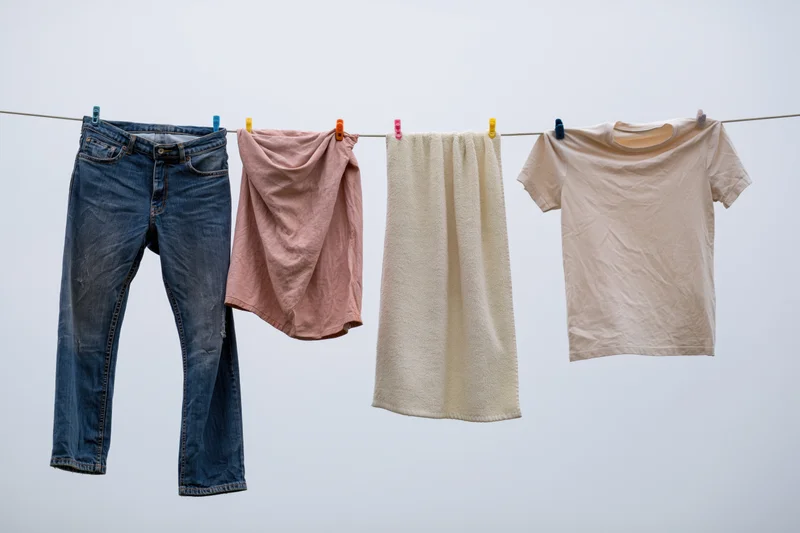 Blue jeans, pink cloth, cream towel and beige tshirt hanging on a clothesline against a light sky