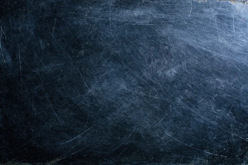 Dark scratched metal surface with worn texture and fine scratches across the frame
