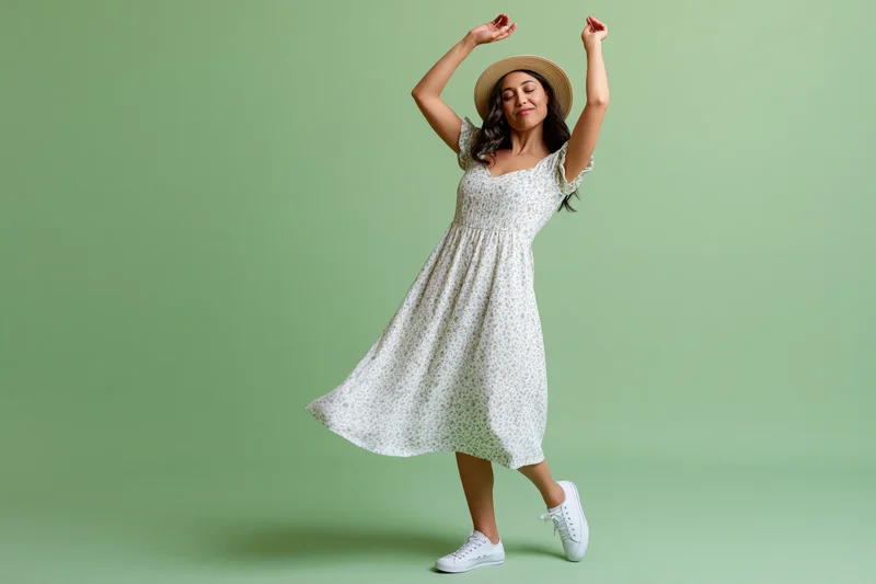 Woman dancing in white floral midi dress and straw hat against green background