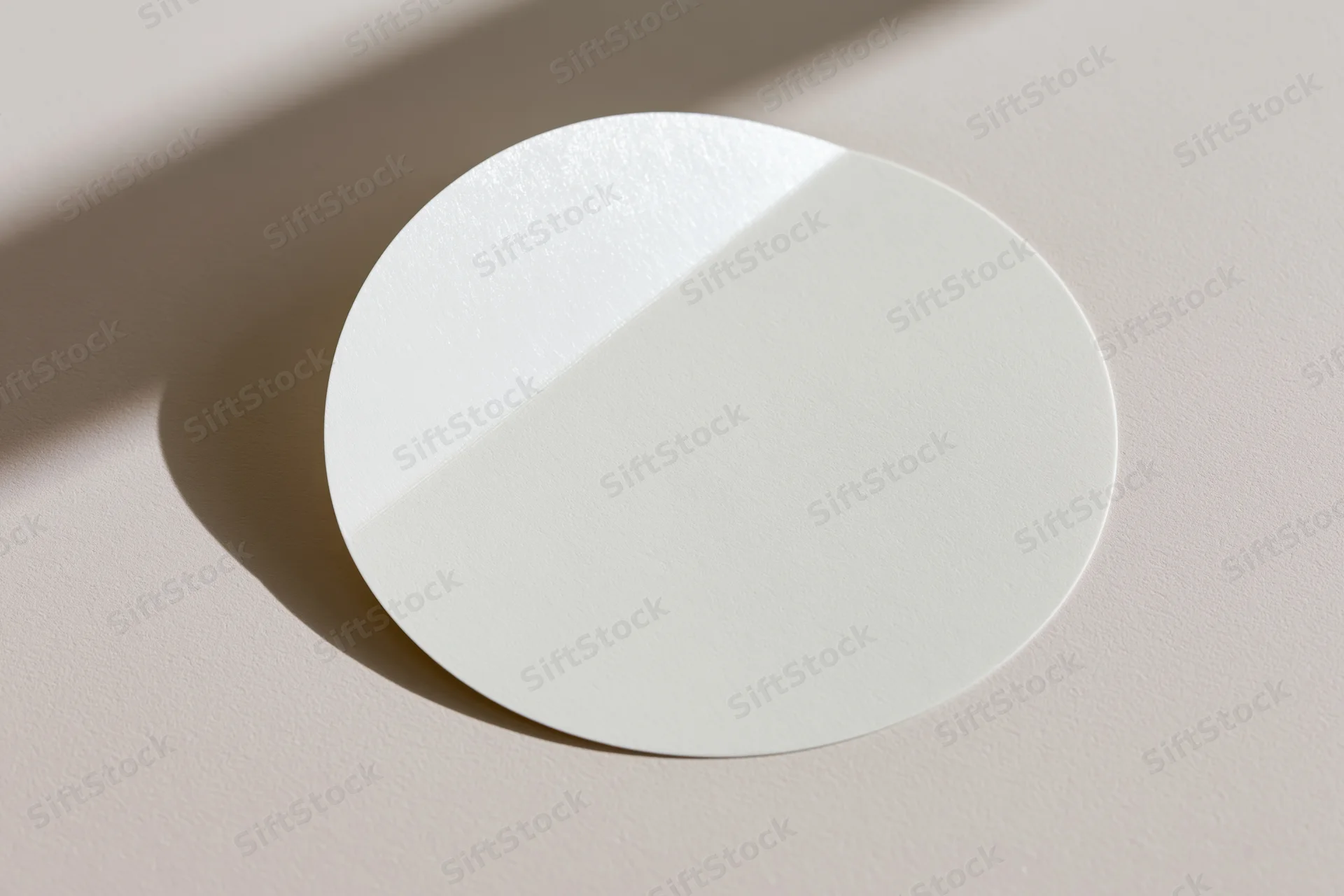 Blank white circular sticker lying flat on a beige surface with soft shadow and copyspace