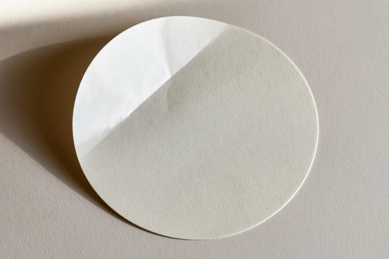 White circular sticker lying flat on a beige surface with soft shadow and copyspace