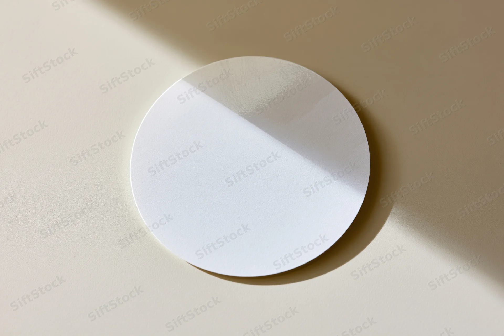 Blank white circular sticker lying flat on a beige surface with soft shadow and copyspace