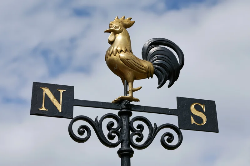 Brass rooster weather vane with wrought iron scrollwork against cloudy sky