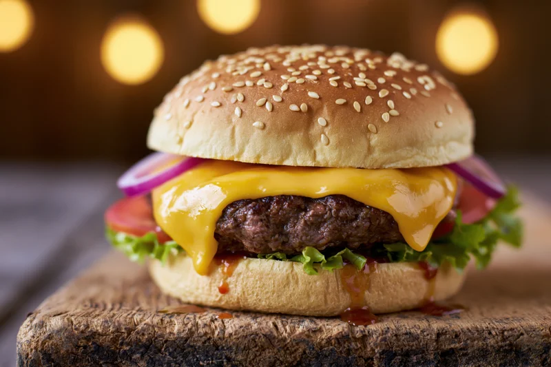 Cheeseburger with melted cheese, lettuce, tomato, and onion on a wooden cutting board