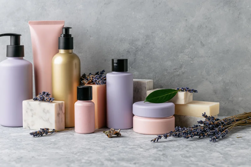 Skincare and beauty product containers arranged with lavender and soap on a gray textured surface