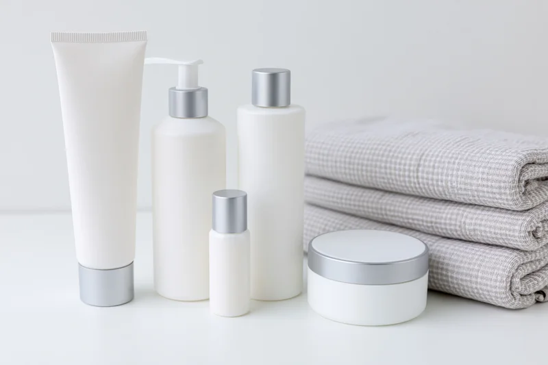 White unlabeled skincare containers and folded towels arranged on a clean surface