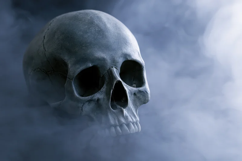 Cracked human skull with detached jaw emerging from thick smoke