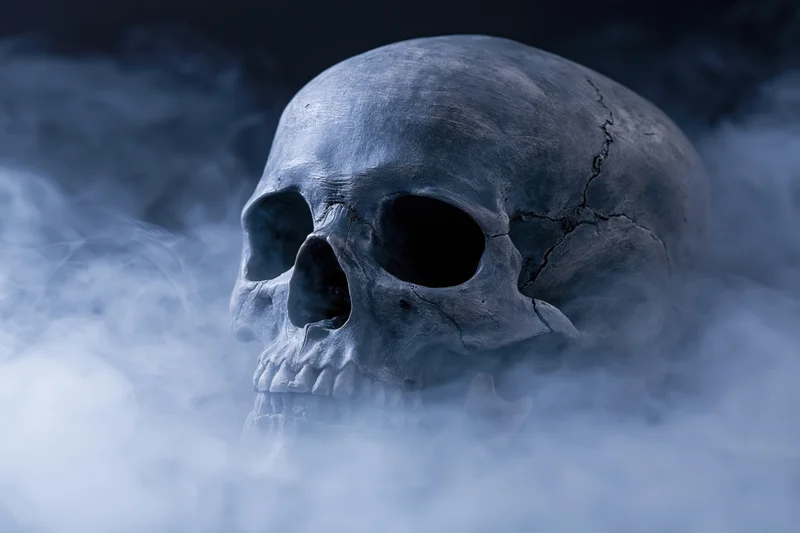 Cracked human skull with detached jaw emerging from thick smoke in dark blue lighting
