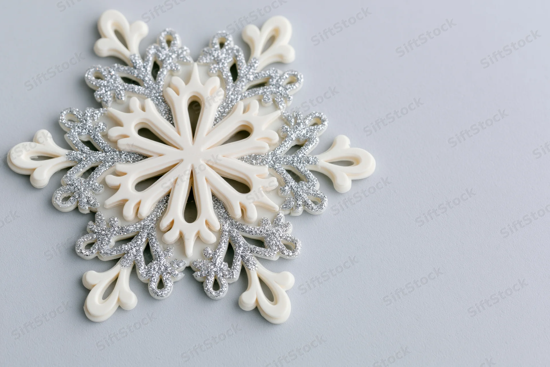 Decorative snowflake ornament with silver glitter details on light grey surface