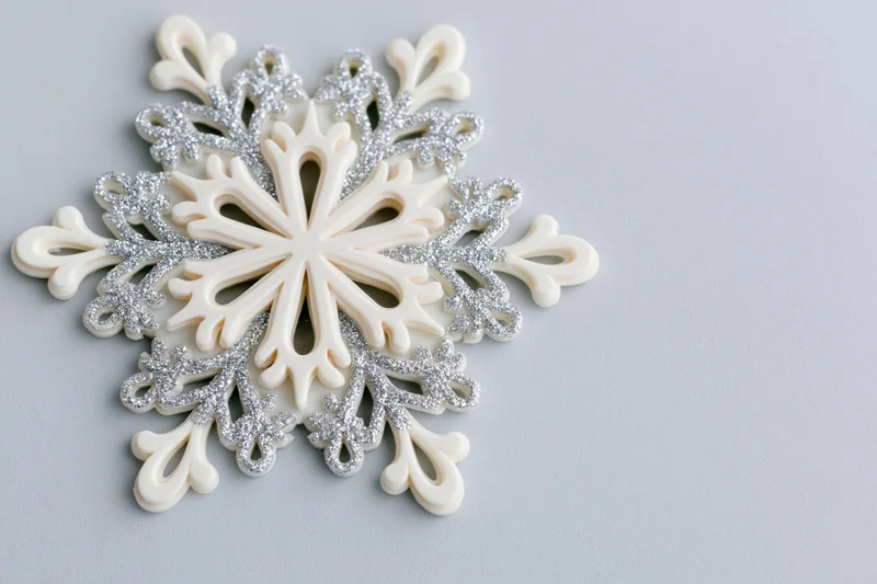 Decorative snowflake ornament with silver glitter details on light grey surface