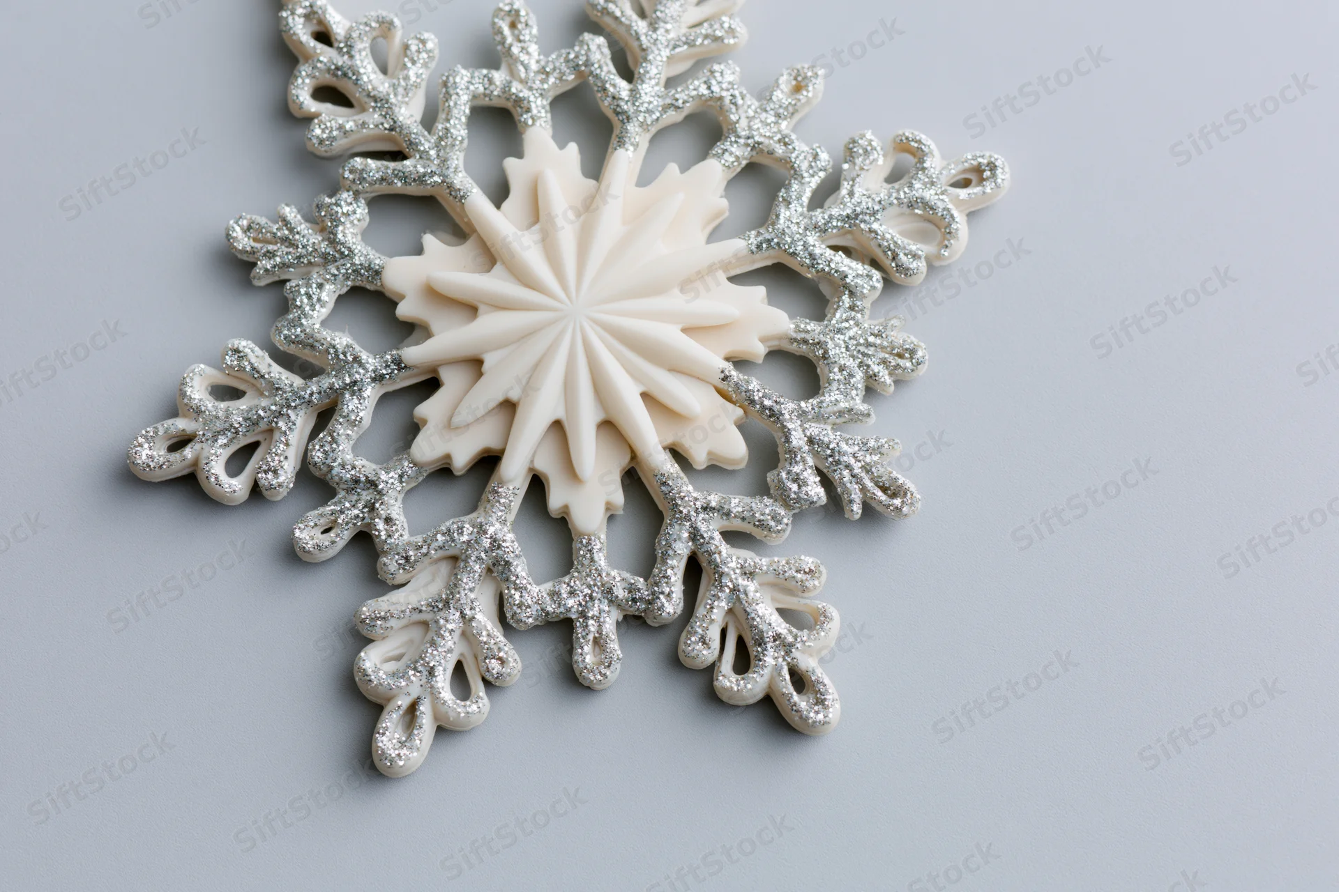 Decorative snowflake ornament with glittered edges resting on light grey surface