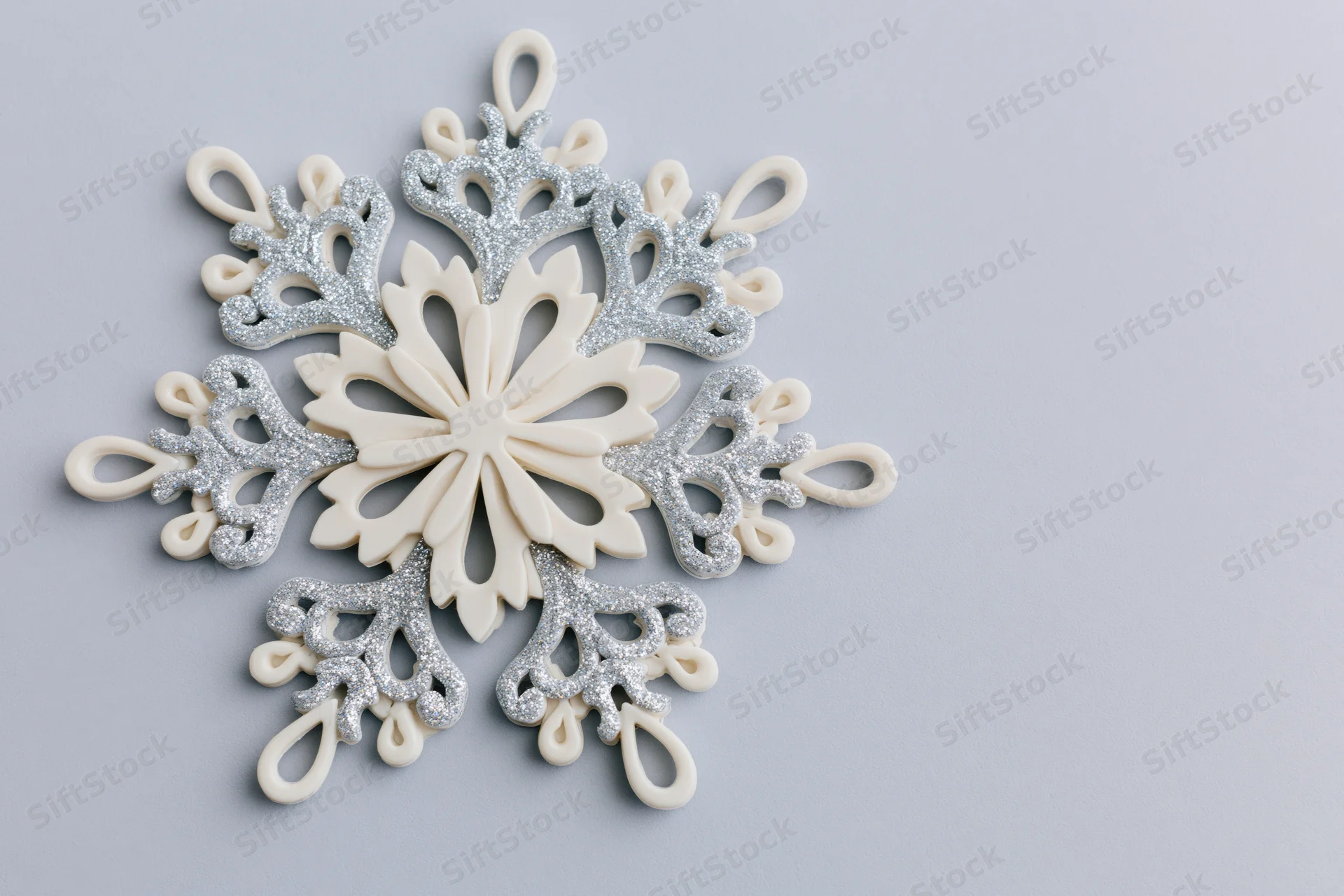 Decorative snowflake ornament with silver glitter details on light grey surface