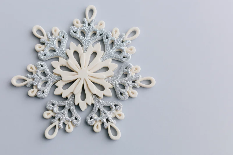 Decorative snowflake ornament with silver glitter details on light grey surface