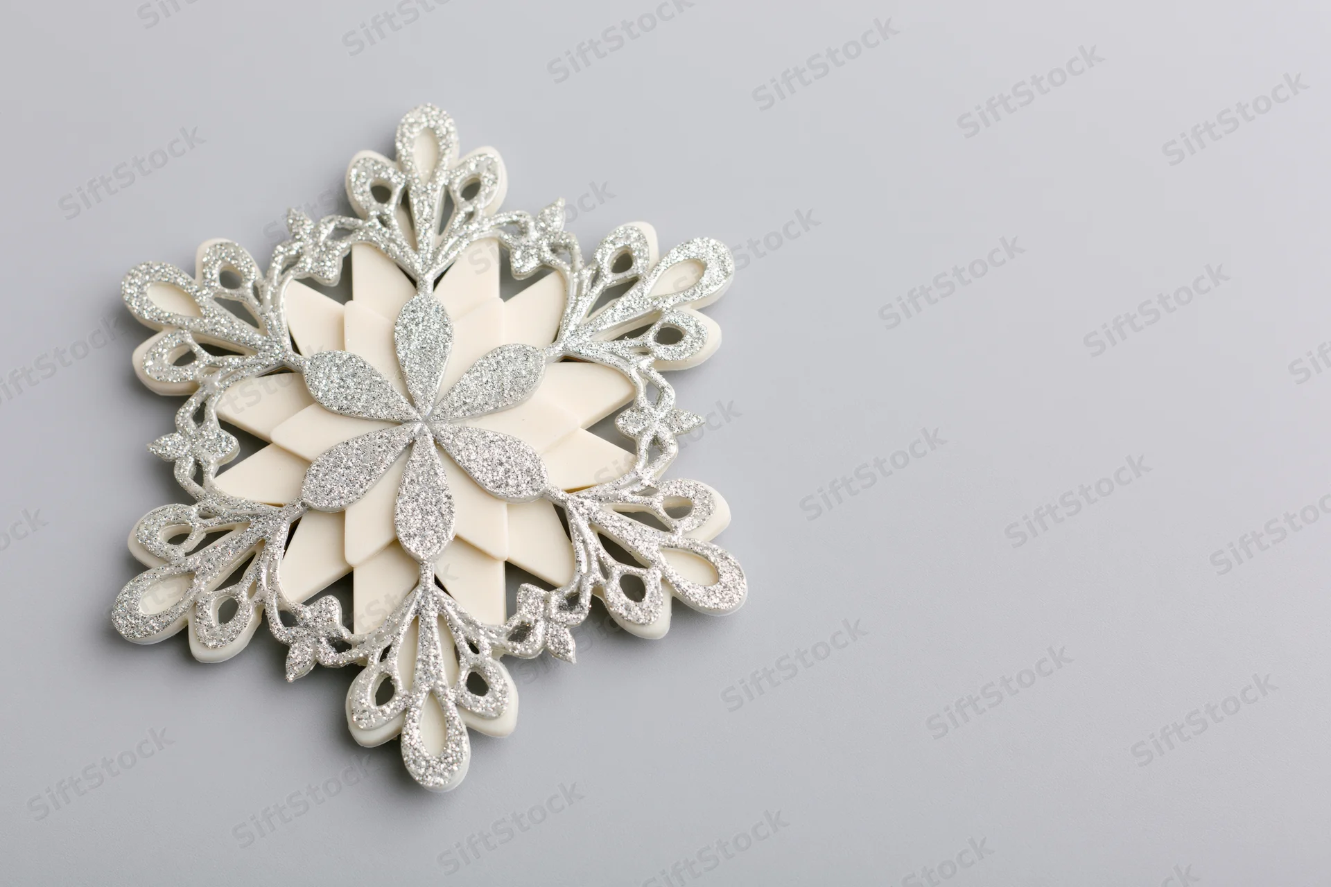 Decorative snowflake ornament with glitter details on a light grey surface