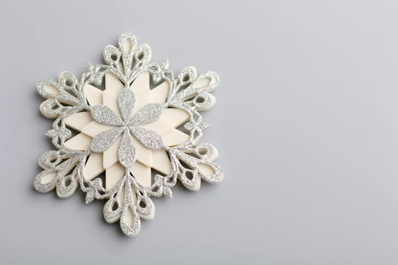 Decorative snowflake ornament with glitter details on a light grey surface