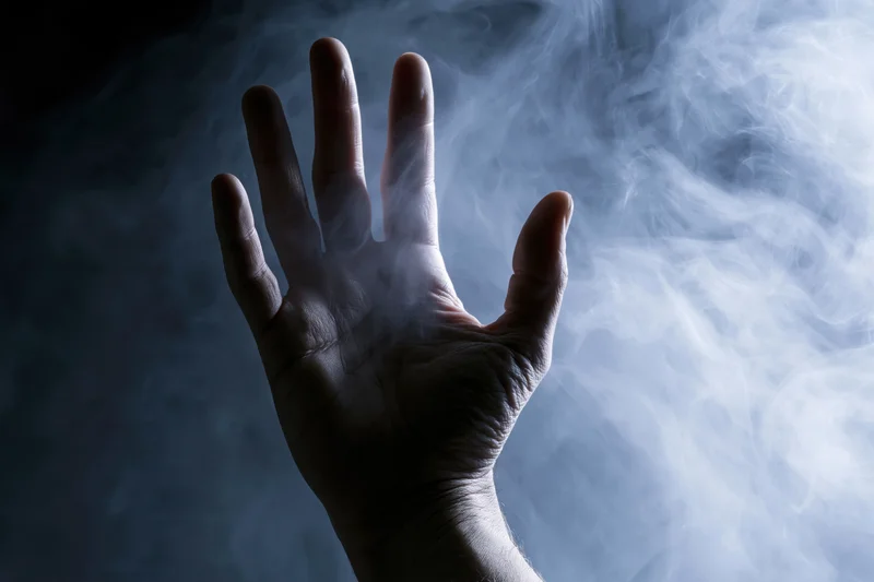 Hand reaching forward with splayed fingers through swirling smoke in dark atmosphere