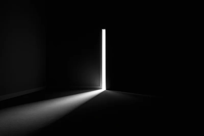 A slightly open door in a dark room letting in a beam of white light