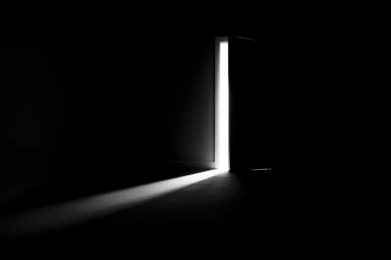 A slightly open door in a dark room letting in a beam of bright white light