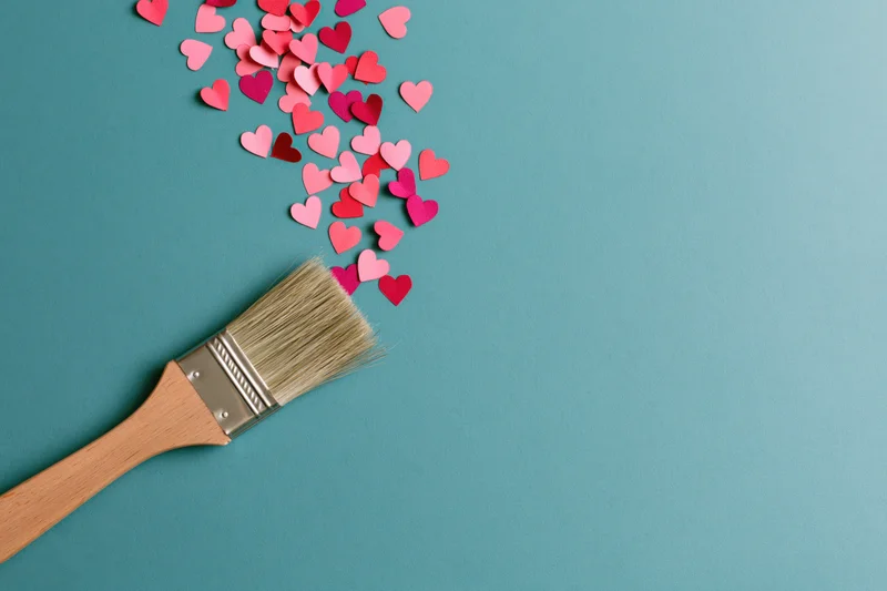 Paintbrush with scattered paper hearts on teal surface