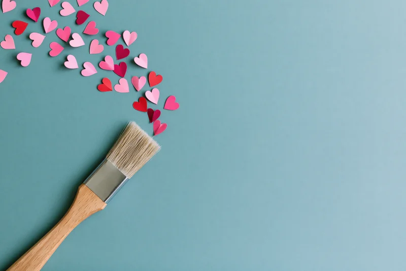 Paintbrush with paper hearts arranged in arc on teal surface
