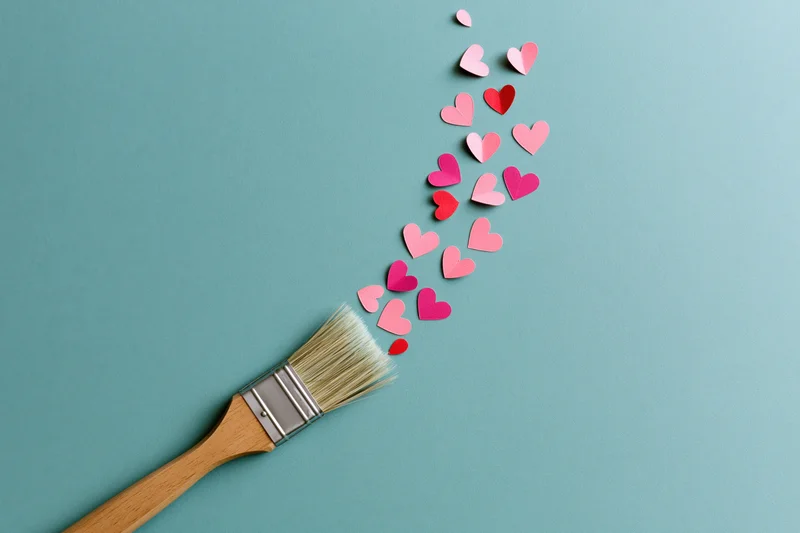 Paintbrush with paper hearts trailing from bristles on teal surface