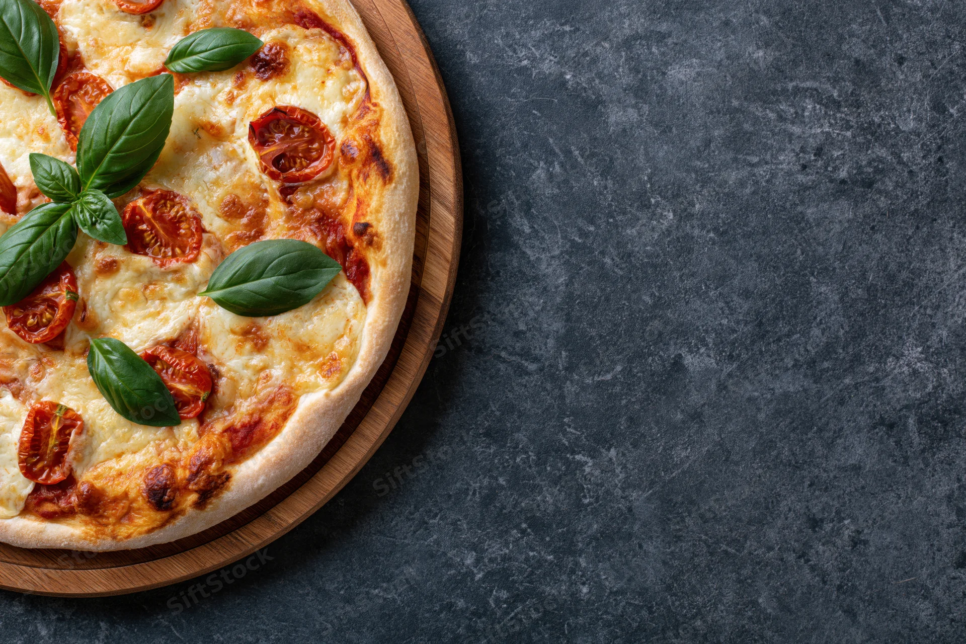 Margherita pizza with mozzarella cheese, cherry tomatoes, and basil leaves on a round wooden serving board, placed on a dark stone surface with copyspace to the right