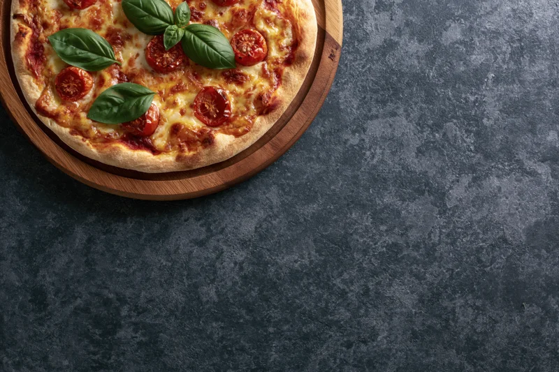 Margherita pizza with fresh basil and tomato slices on a wooden tray on dark stone surface