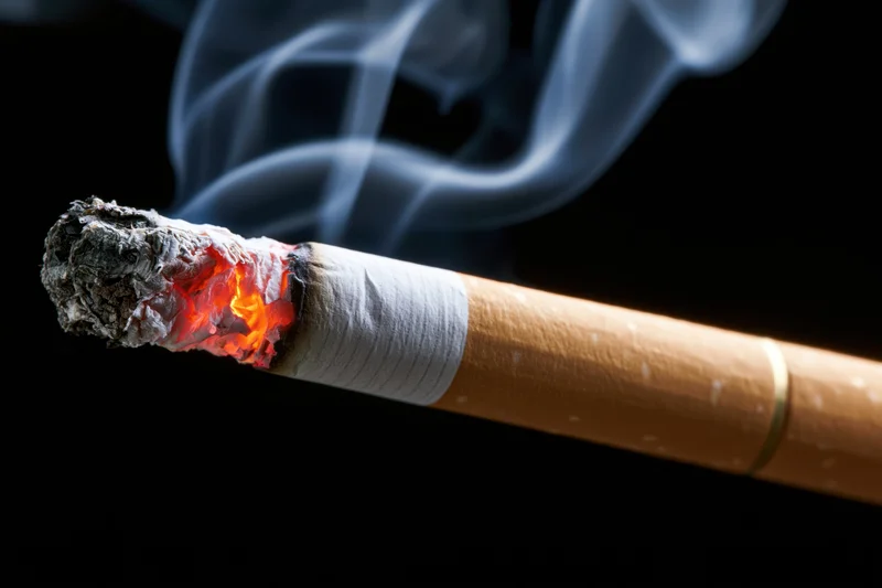 Lit cigarette with glowing ember and rising smoke against black background