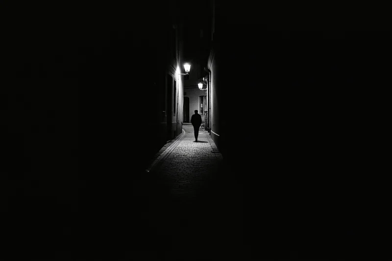 Silhouette of a person walking away down a narrow cobblestone alley at night