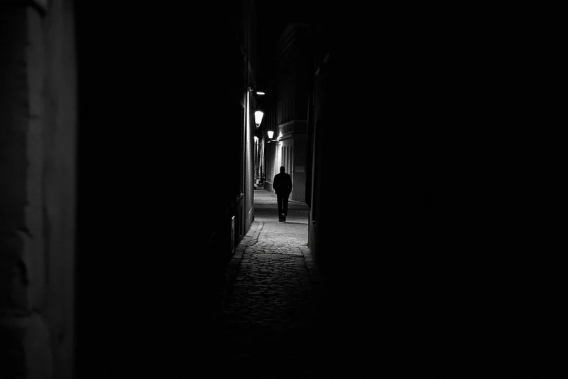 Silhouette of a person walking away down a narrow cobblestone alley at night