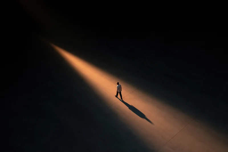 Man walking forward on dark concrete under a beam of light