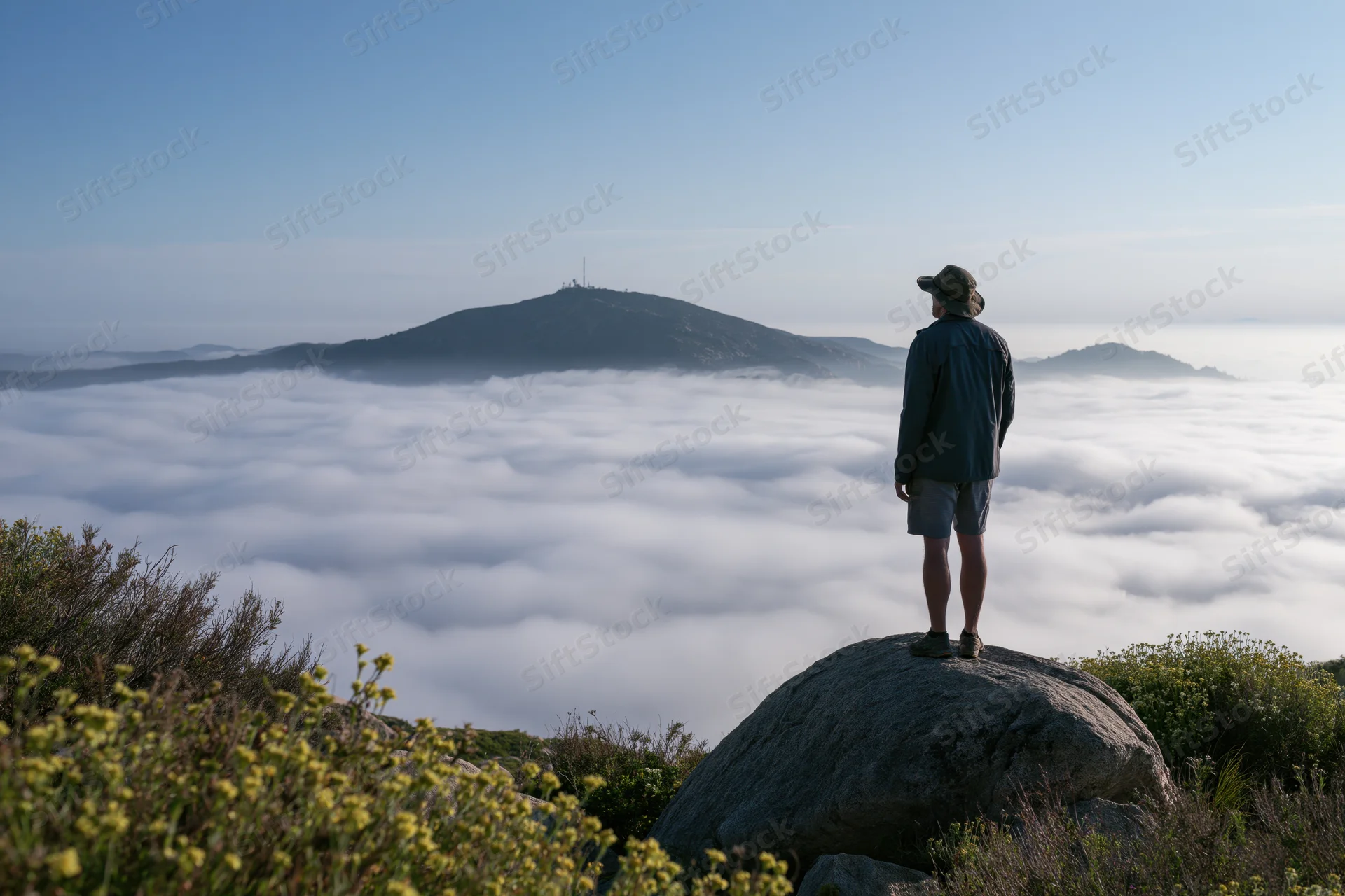 Hiker standing on a granite boulder overlooking a vast sea of clouds below a mountain peak