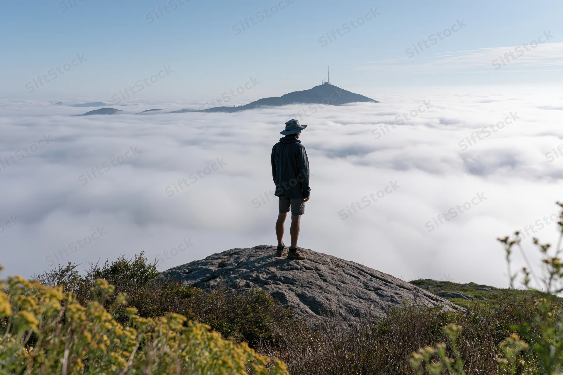 Male hiker standing on granite boulder overlooking sea of clouds from mountain summit