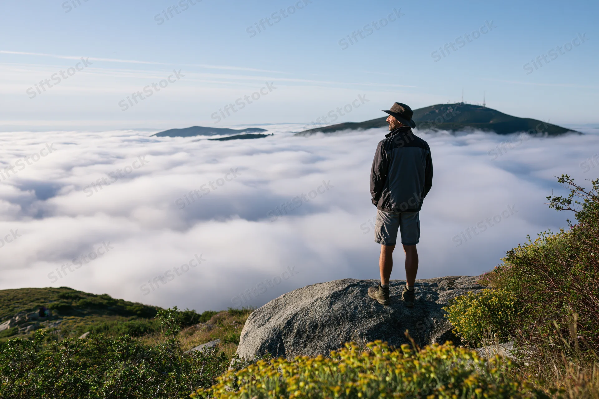 Hiker standing on granite boulder overlooking sea of clouds from mountain summit