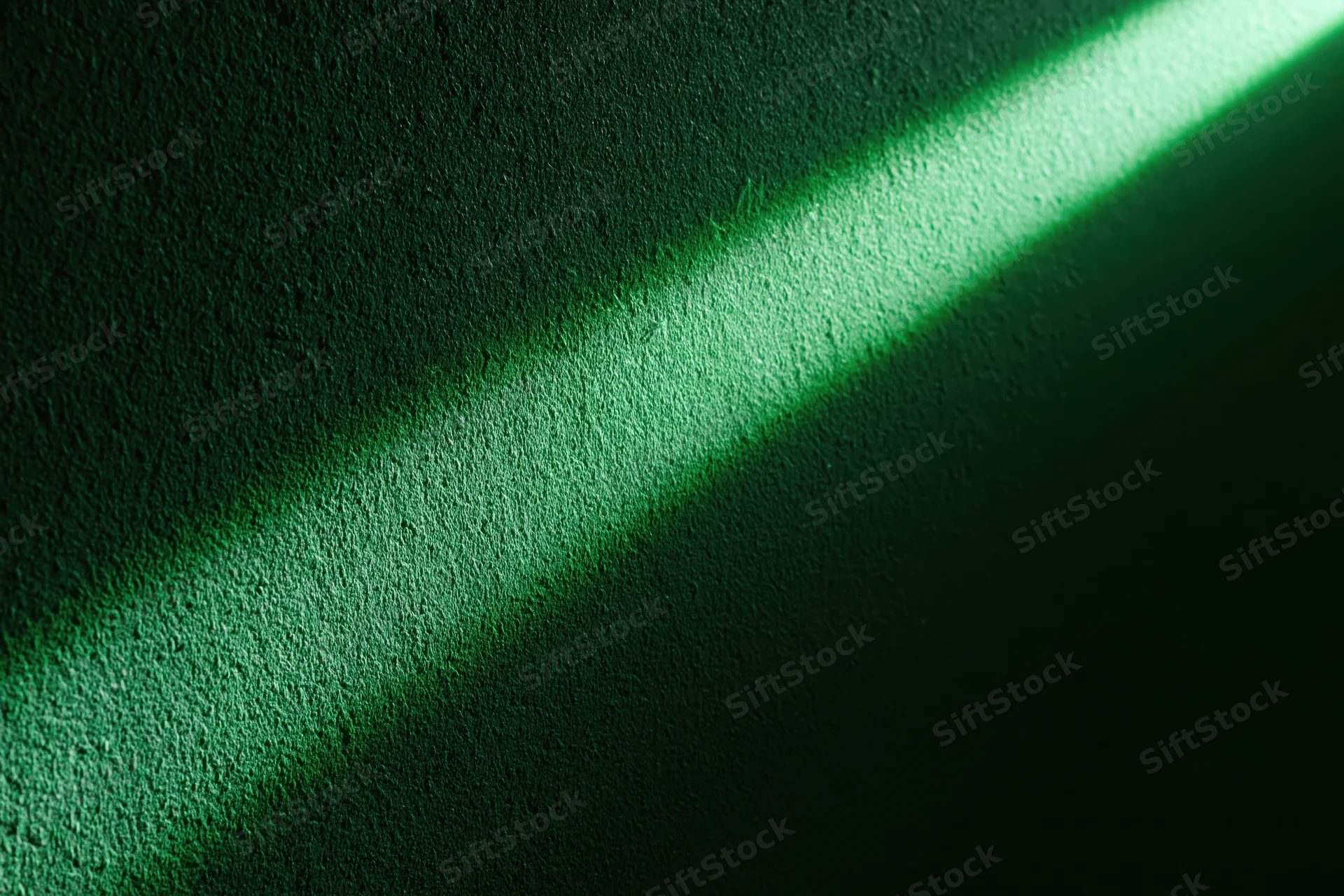 Narrow beam of green light striking a rough textured wall in a dark interior