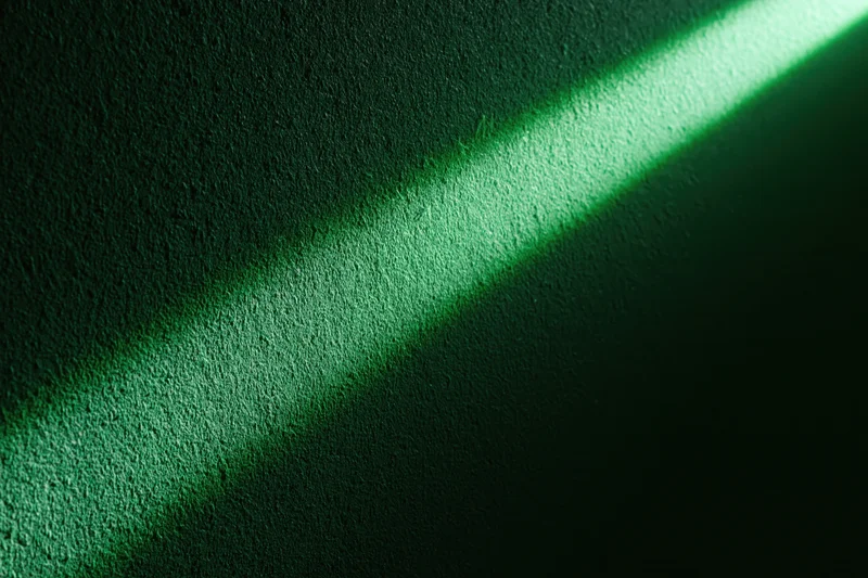 Narrow beam of green light striking a rough textured wall in a dark interior