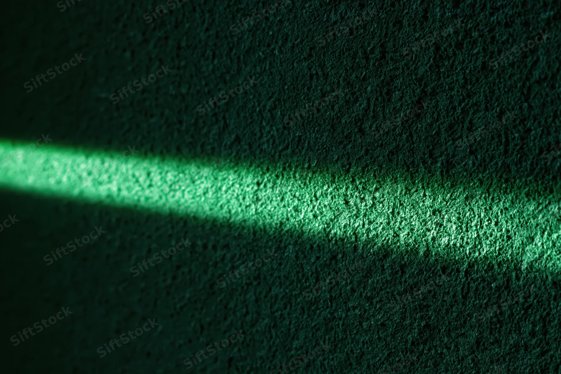 Narrow beam of green light striking a rough textured wall in a dark interior