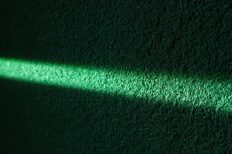 Narrow beam of green light striking a rough textured wall in a dark interior