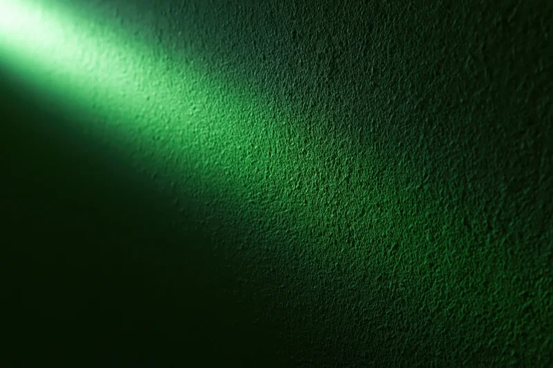Narrow beam of green light striking a rough textured wall