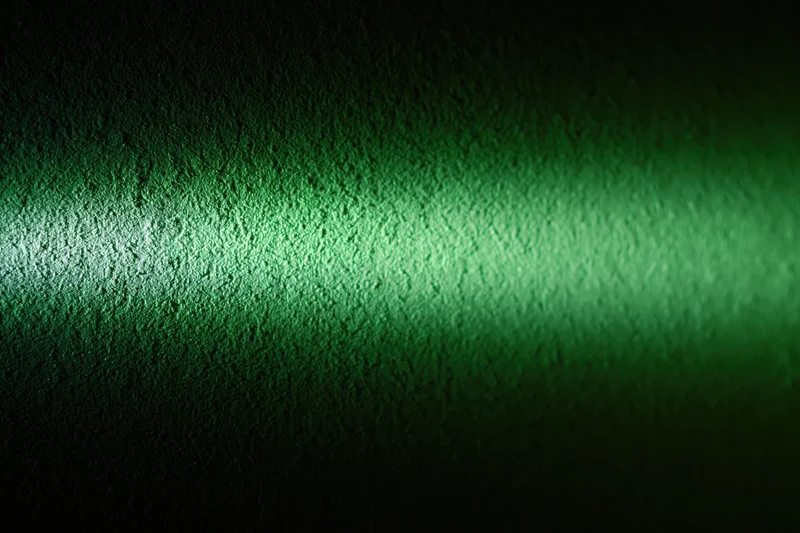 Narrow beam of green light striking a rough textured wall