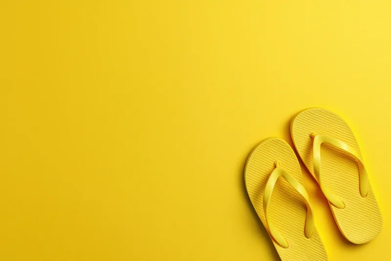 Yellow rubber flip-flops placed in bottom-right corner on matching yellow background