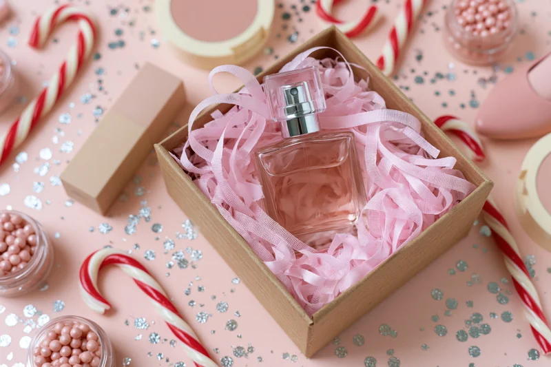 Pink perfume bottle in a kraft gift box surrounded by candy canes and glitter on a pink surface