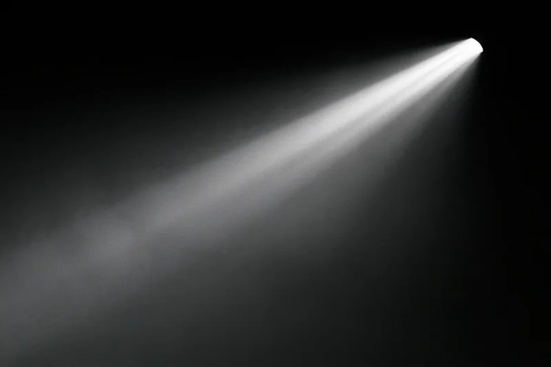 A single beam of cool white light cutting diagonally across a dark stage with smoke