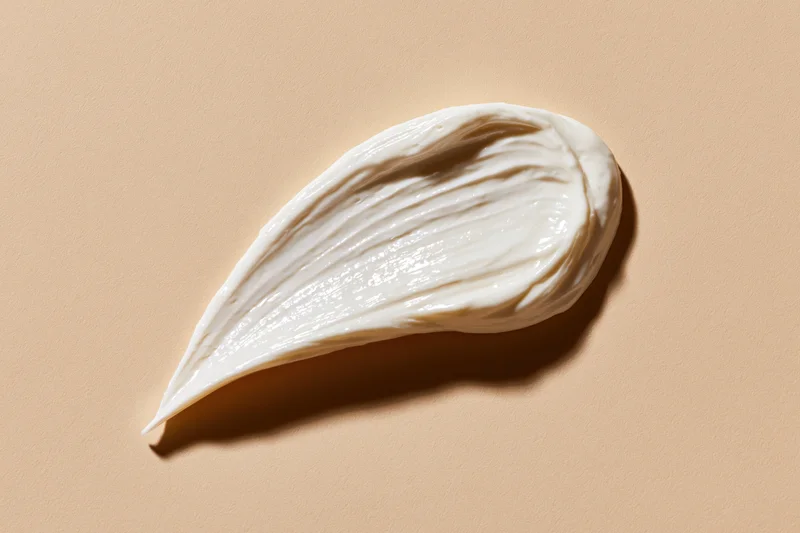 Smooth white cream smear shaped like a tear on a beige background