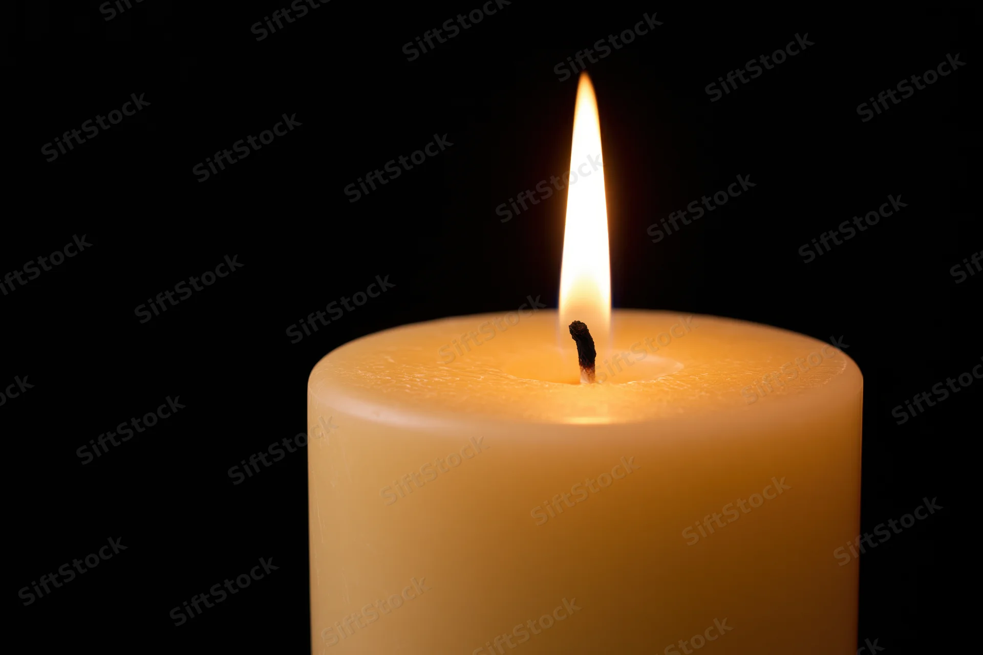 Thick pillar candle burning steadily with upright flame against black background