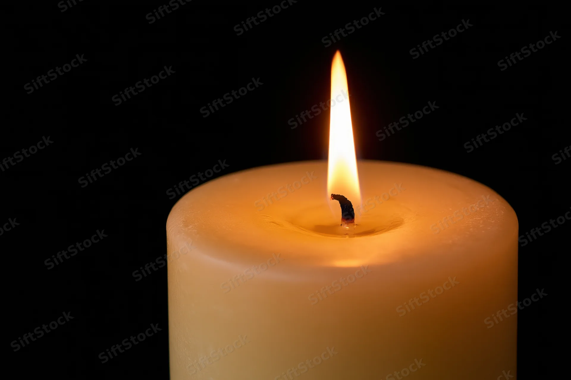 Thick pillar candle burning steadily with upright flame against black background