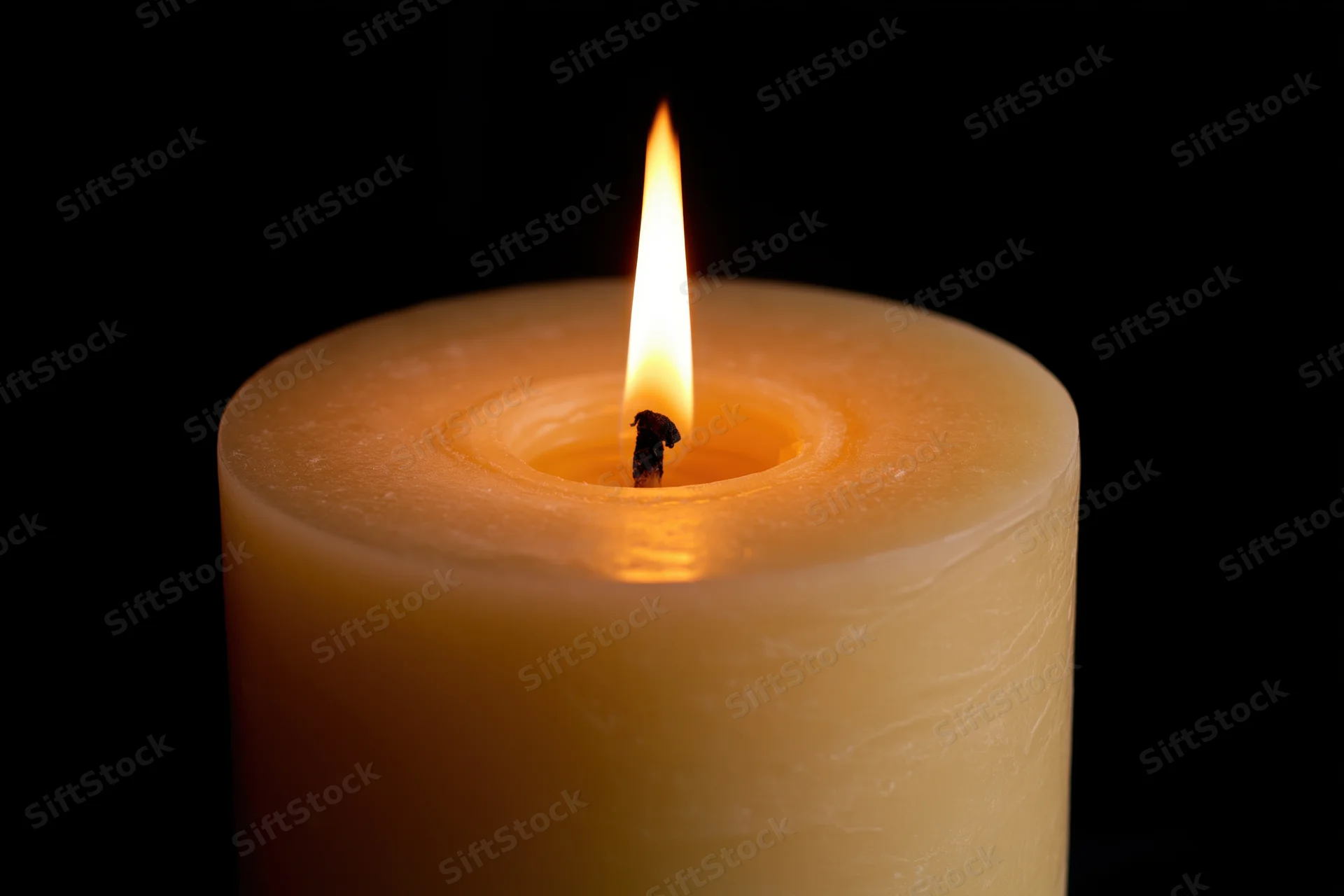 Thick pillar candle burning steadily with upright flame against black background