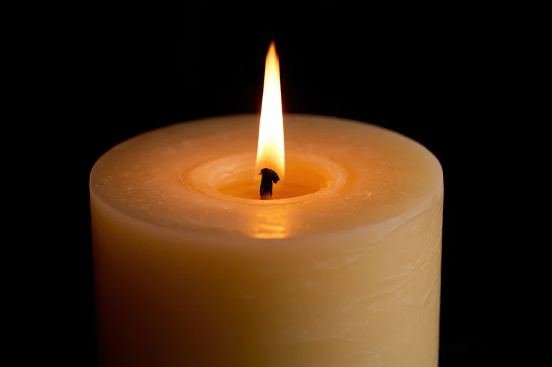 Thick pillar candle burning steadily with upright flame against black background